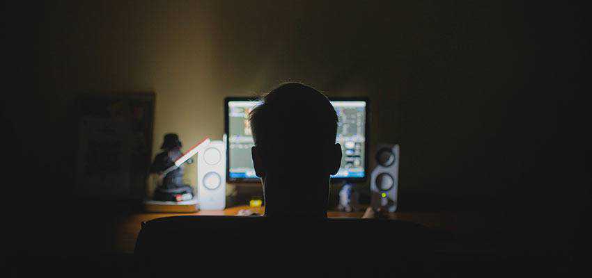 Un hombre sentado frente a una computadora en la oscuridad.