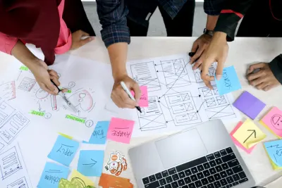 Une photo avec le groupe de personnes autour de la table avec divers autocollants colorés et des notes dessus avec des idées pour la conception de l'interface.