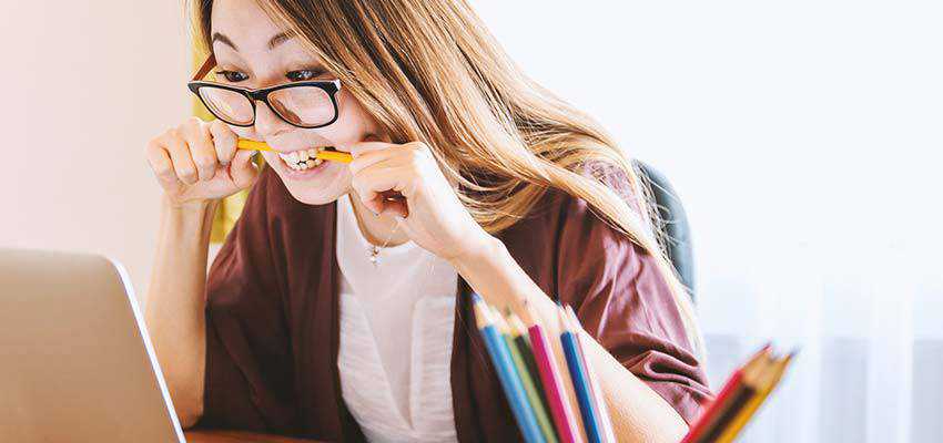 Wanita frustrasi melihat layar komputer sambil mengunyah pensil.